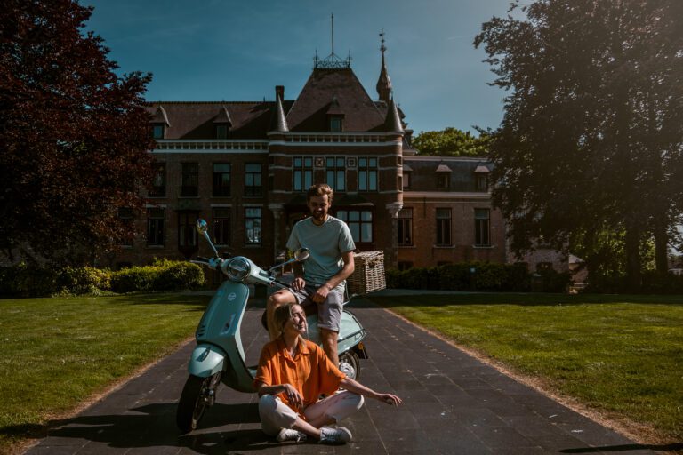 zwei Personen, die mit einer Vespa vor einem schönen Gebäude sitzen